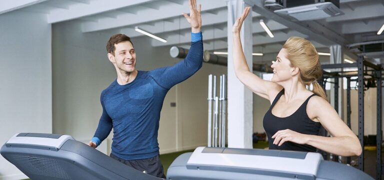 Happy man and woman doing high five during treadmill exercise at gym